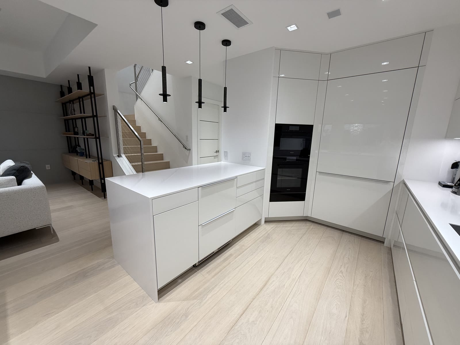 A white modern kitchen with handleless cabinets and a floating stair beyond