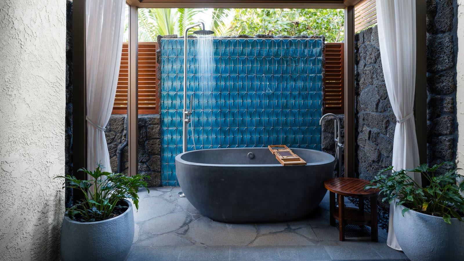 An open-air garden bath with a stone tub, rain shower and blue tile wall