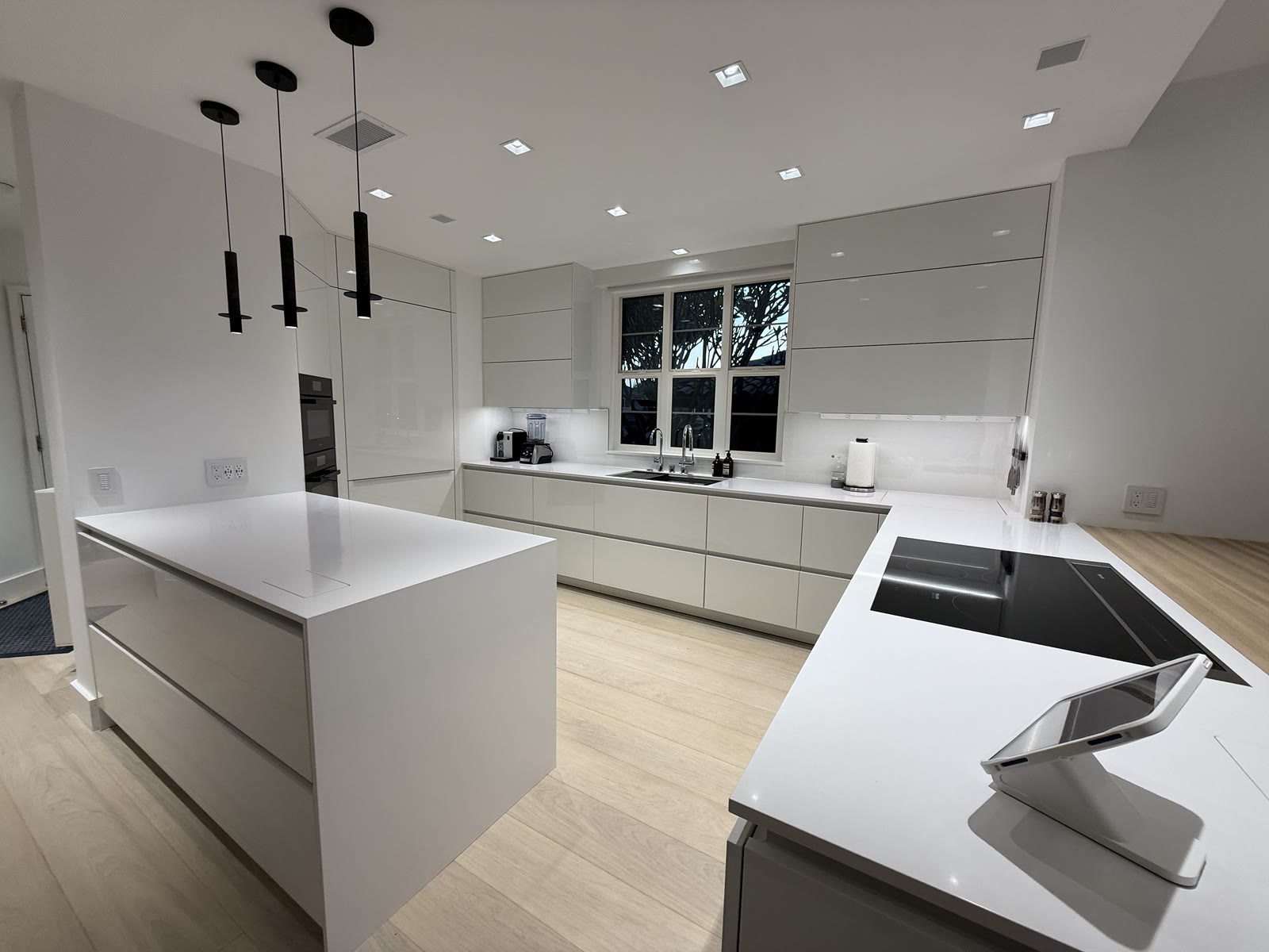 A modern white kitchen with an induction island and black pendants