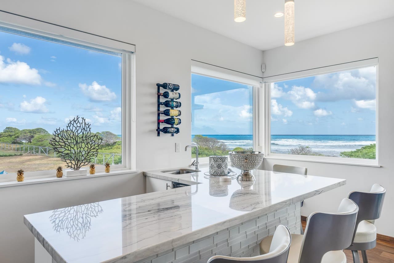 A stone kitchen counter looking out through corner windows to the ocean